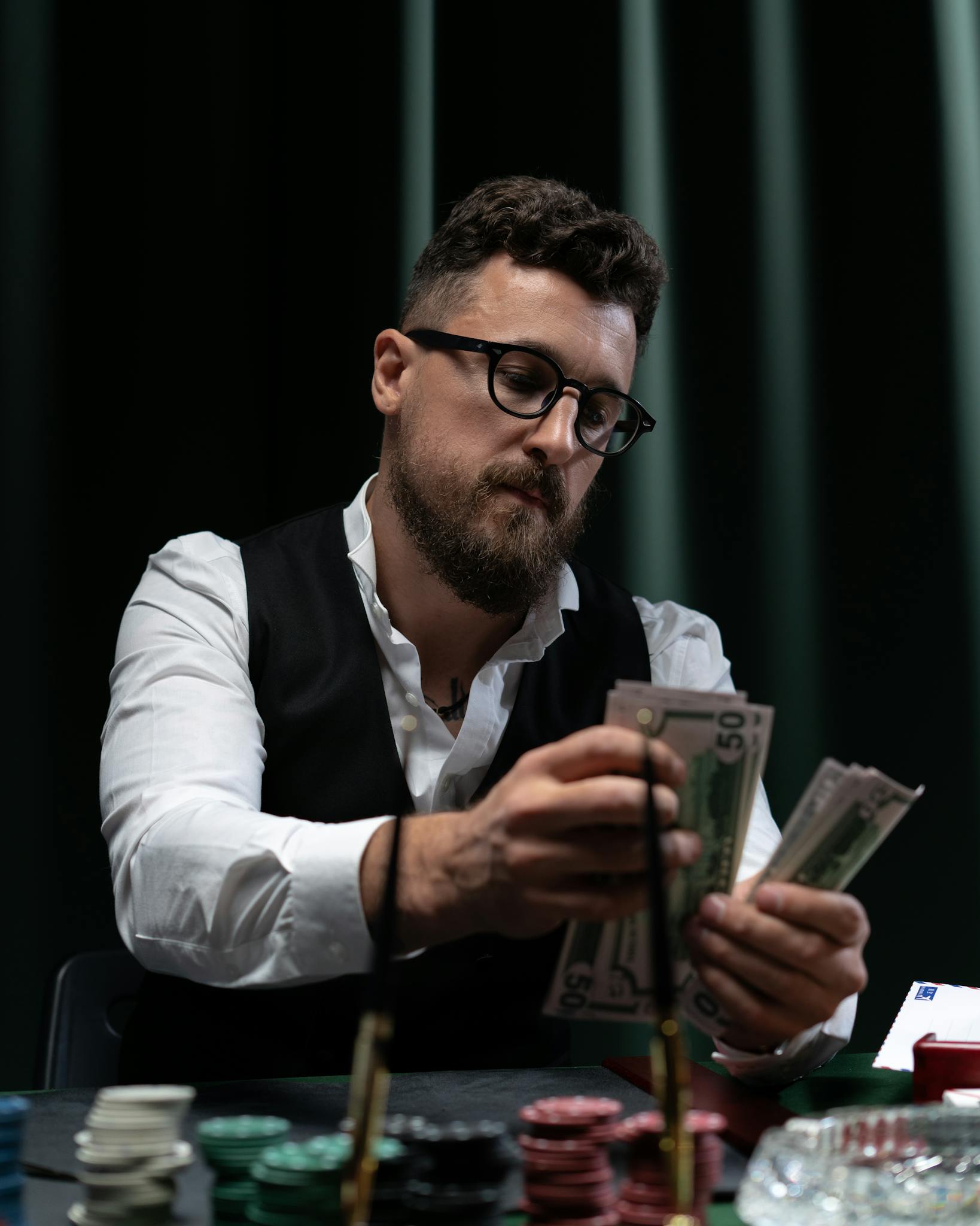 Bearded man in glasses counting money at a poker table, highlighting gambling and finance themes.